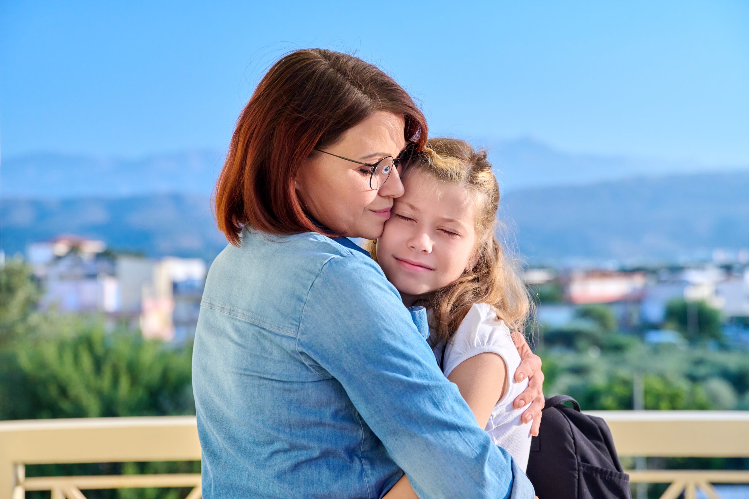 Mom hugging her preteen daughter on the porch of the house